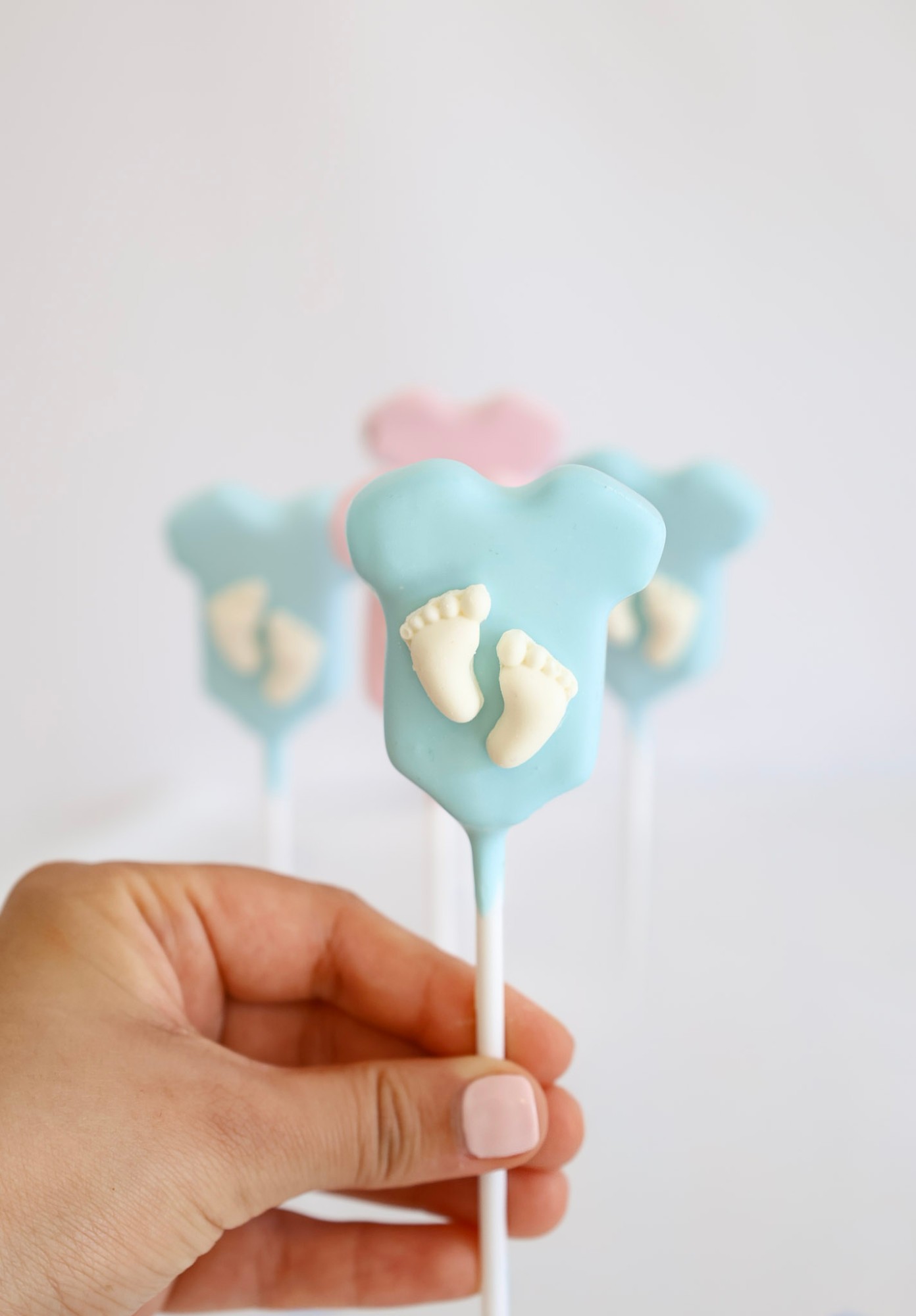 Close-up of a blue baby onesie shaped cake pop with white chocolate feet detail