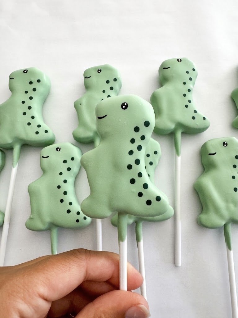 Green dinosaur-shaped cake pops with hand-painted spots and faces