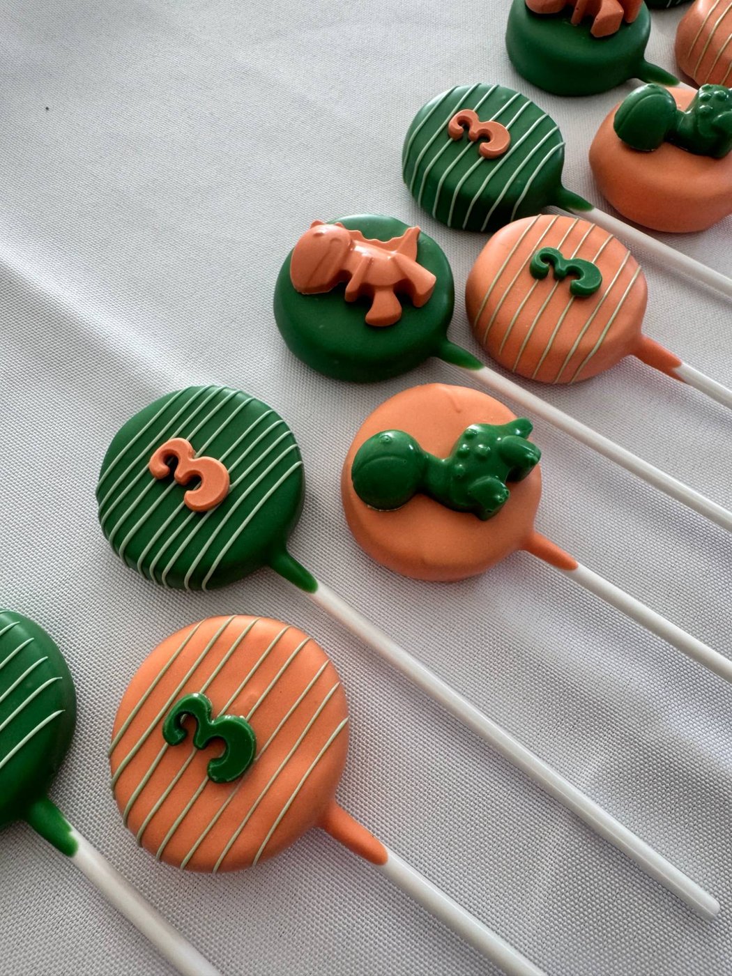 Dinosaur third birthday cake pops in green and orange with number 3 toppers