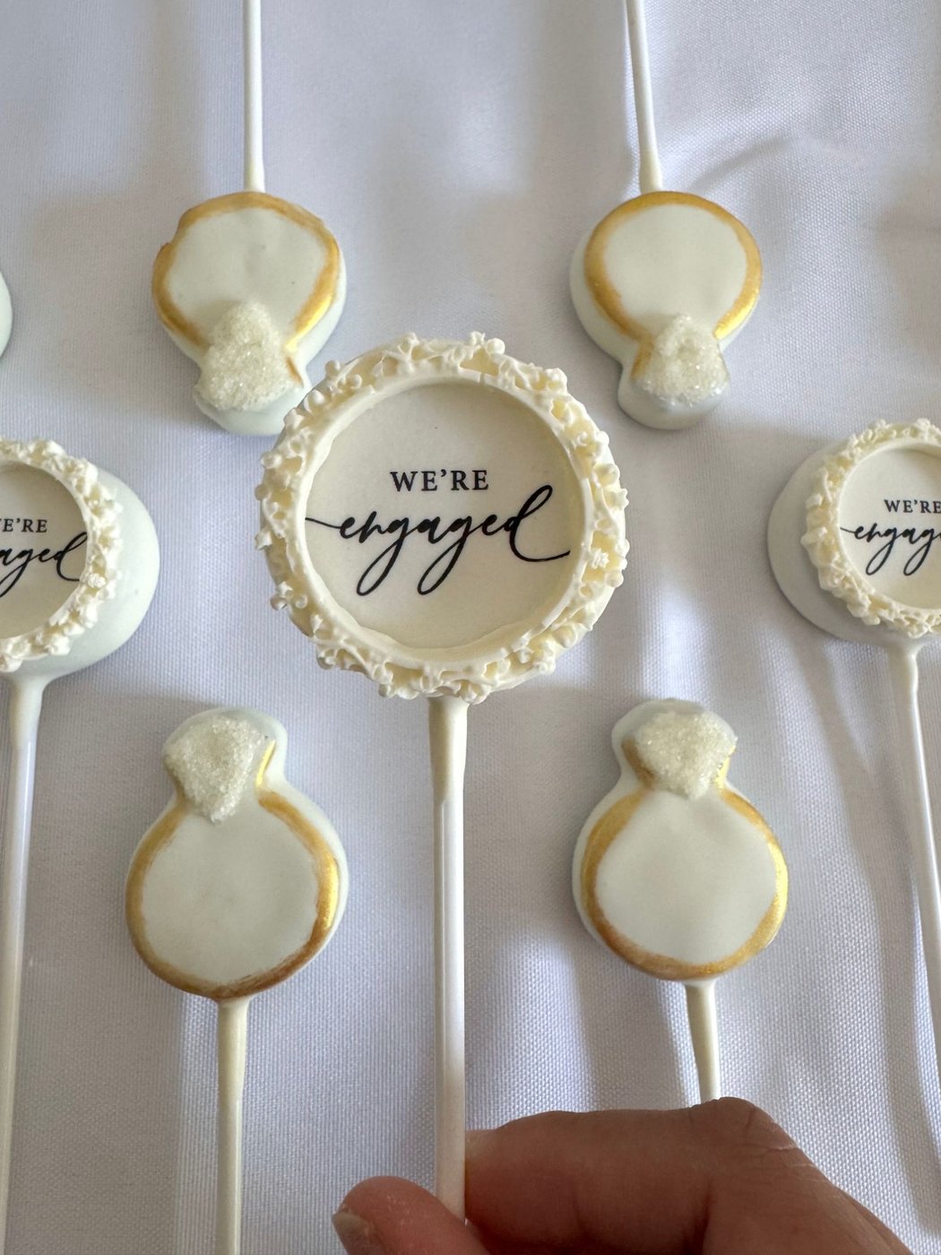 Engagement ring shaped cake pops in white and gold, with a We're Engaged topper