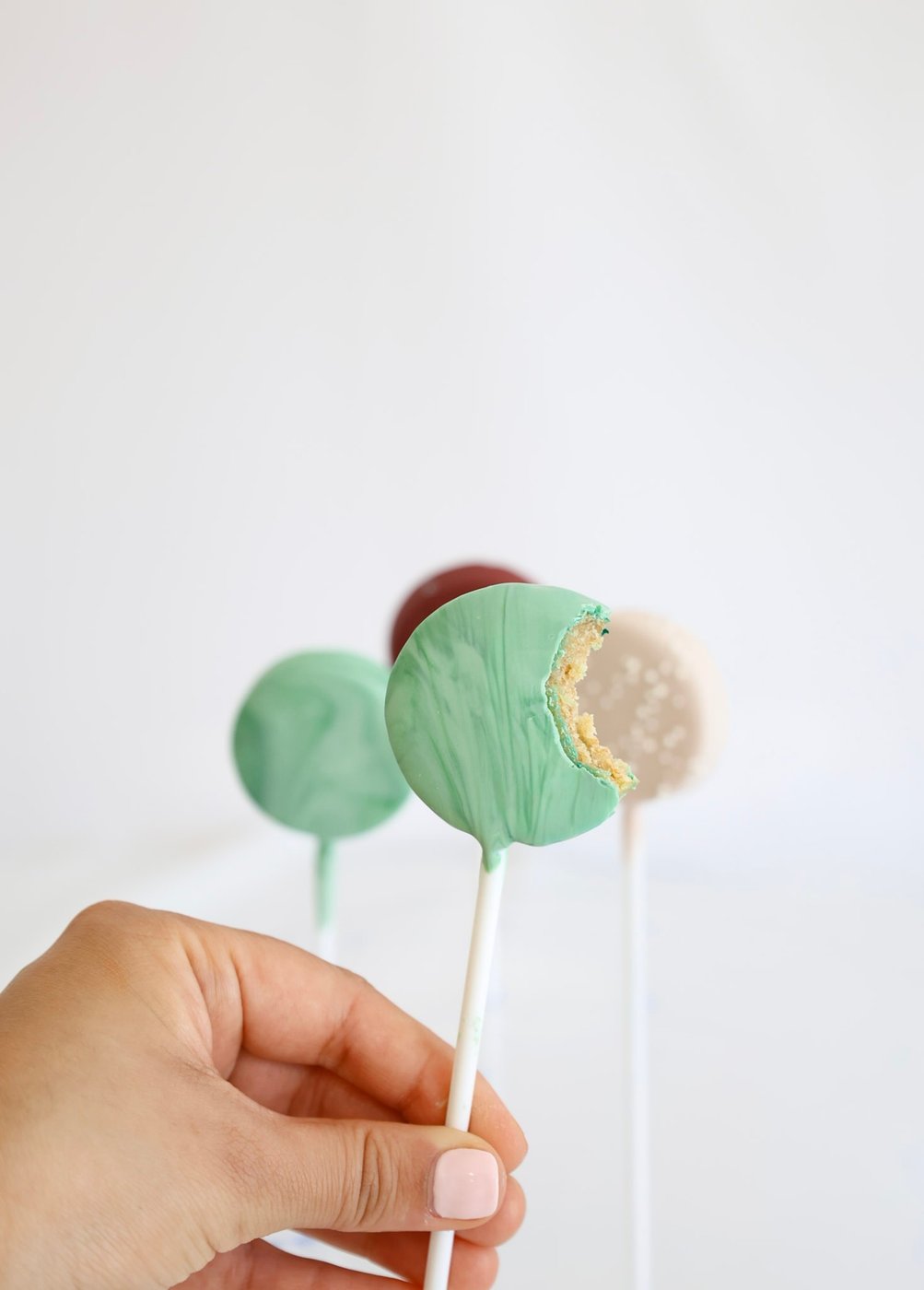 A green marble cake pop with a bite taken out, held in hand with more cake pops blurred in the background
