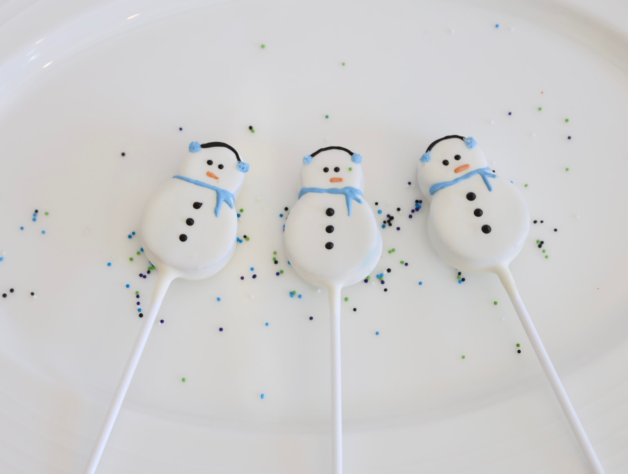 Snowman-shaped cake pops decorated with earmuffs, a scarf, and a carrot nose