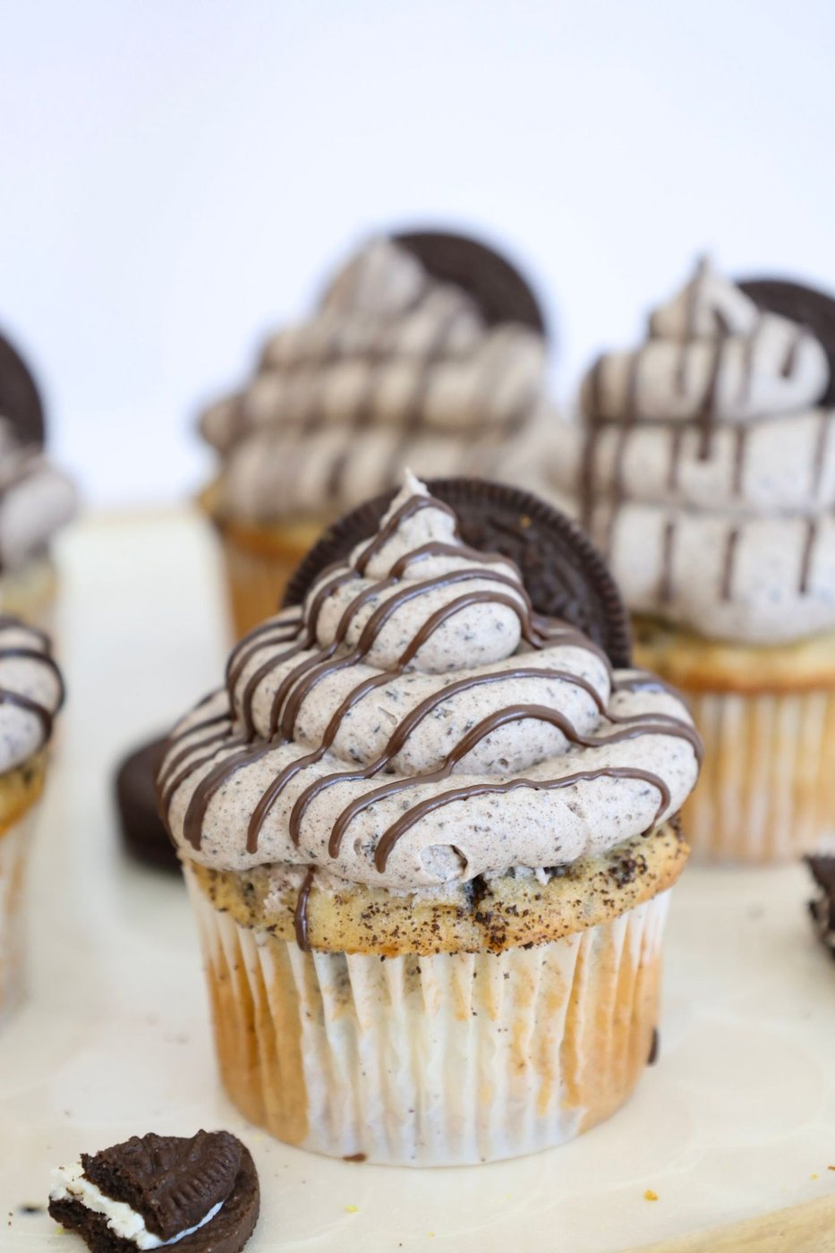 Close-up of a cookies and cream cupcake with Oreo crumb frosting, an Oreo cookie, and a chocolate drizzle