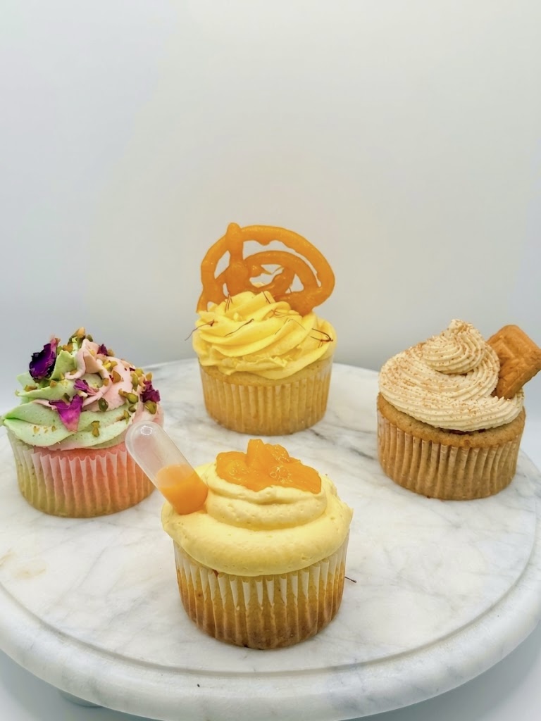 Four Indian-fusion gourmet cupcakes on a marble stand: Pistachio Rose, Jalebi & Rabdi, Mango Lassi, and Kadak Chai