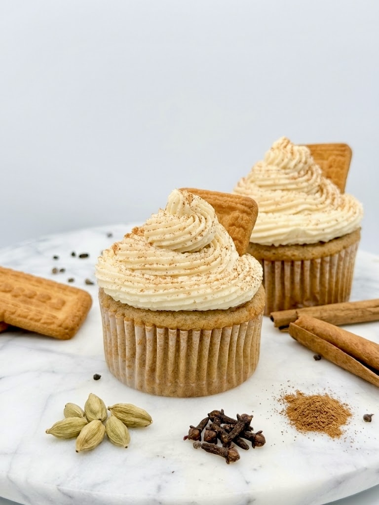 Kadak Chai cupcakes with spiced cream swirls and Parle-G biscuits, surrounded by cardamom, cloves, and cinnamon
