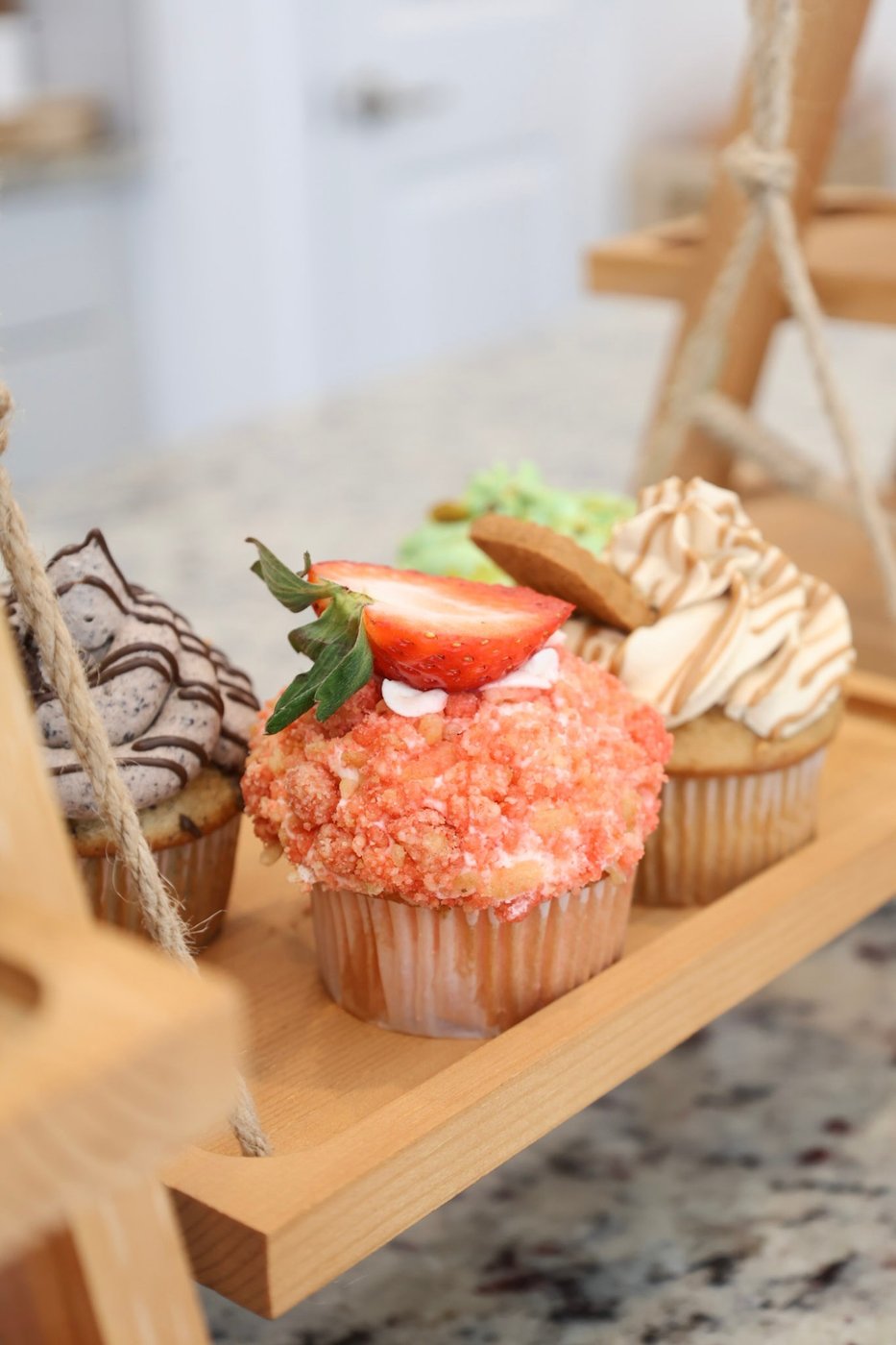 Cookies and cream, strawberry crunch, and Biscoff cupcakes displayed on a wooden swing stand