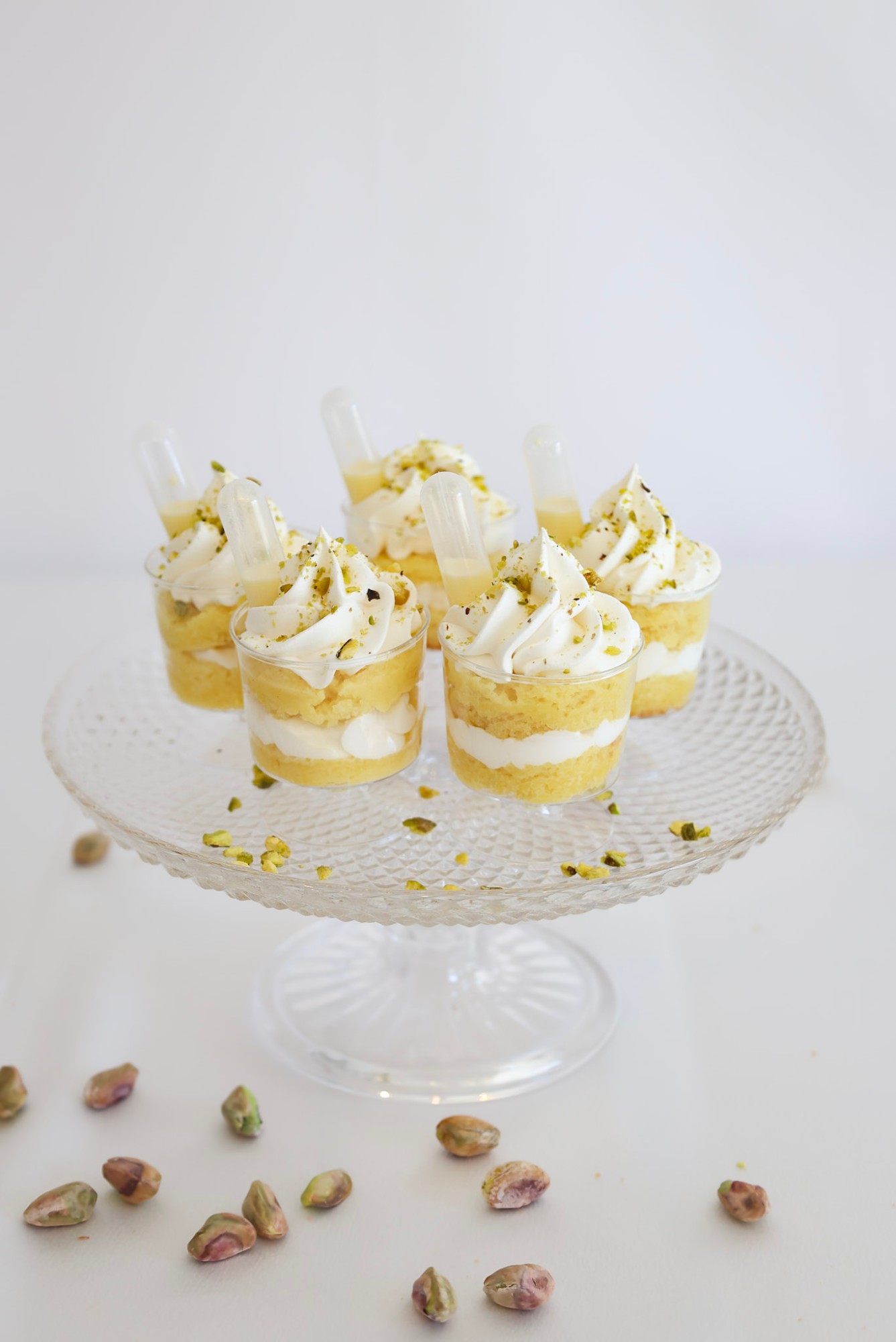 Pistachio dessert cups topped with whipped cream and crushed pistachios on a glass cake stand