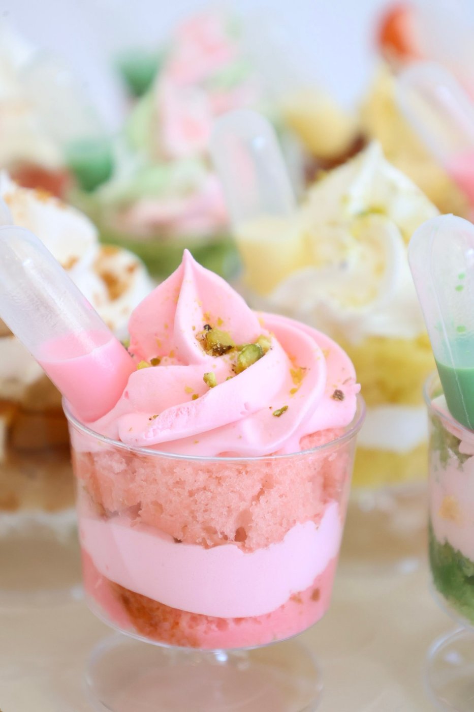 Close-up of a strawberry shortcake dessert cup topped with pink whipped cream and crushed pistachio