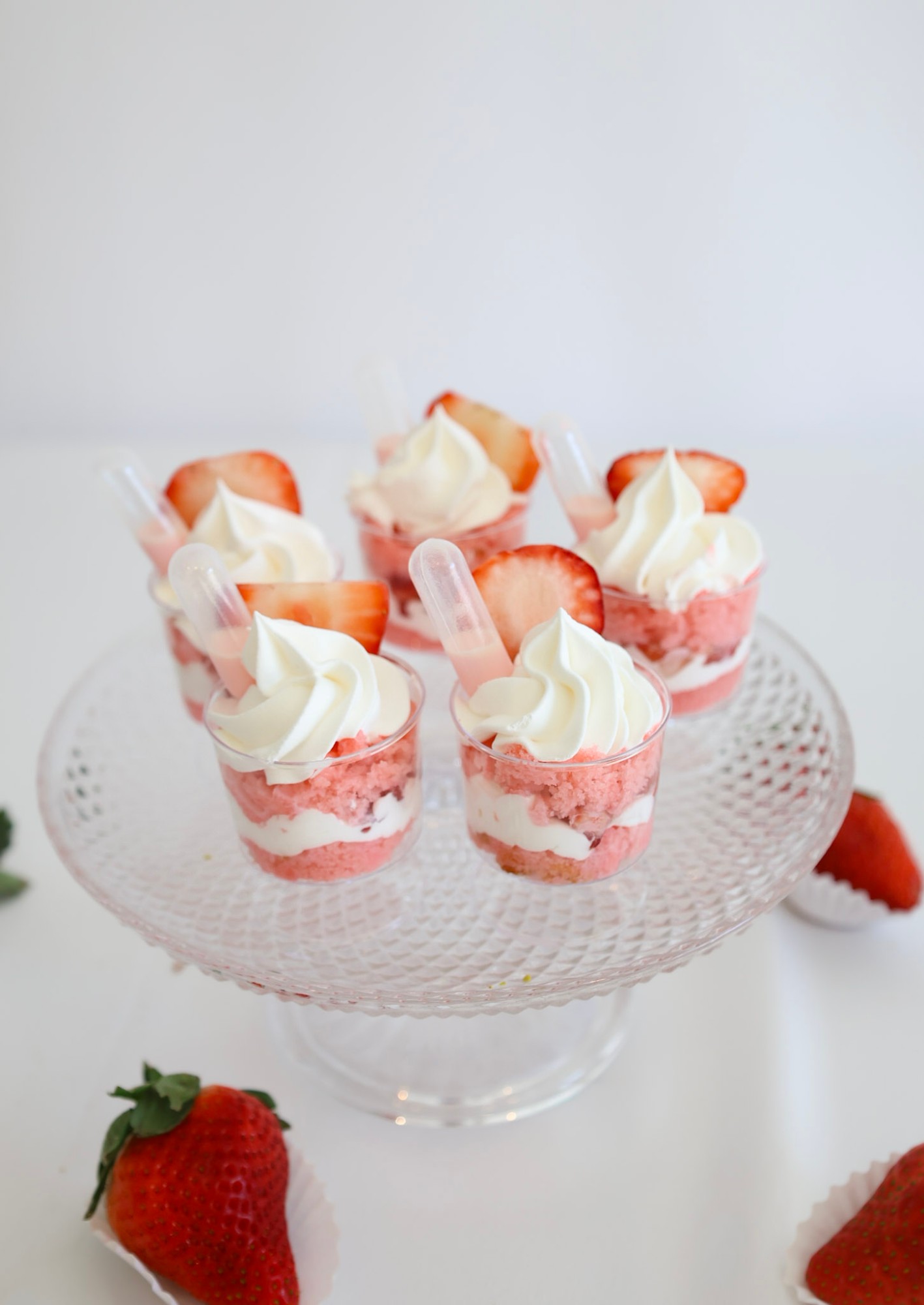 Strawberry shortcake dessert cups topped with whipped cream on a glass cake stand