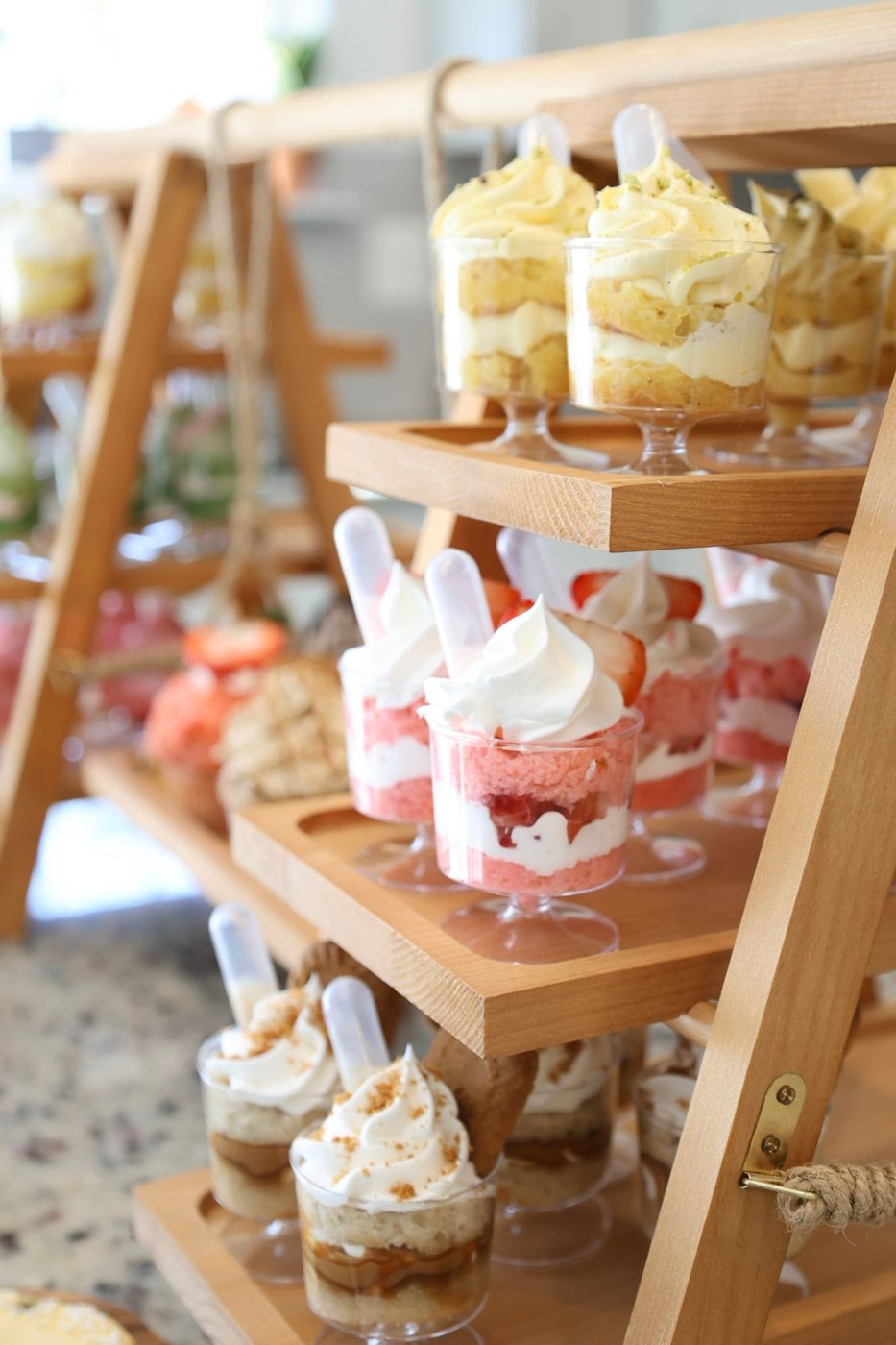 A tiered wooden ladder stand displaying assorted dessert cups in pistachio, strawberry, and Biscoff flavors
